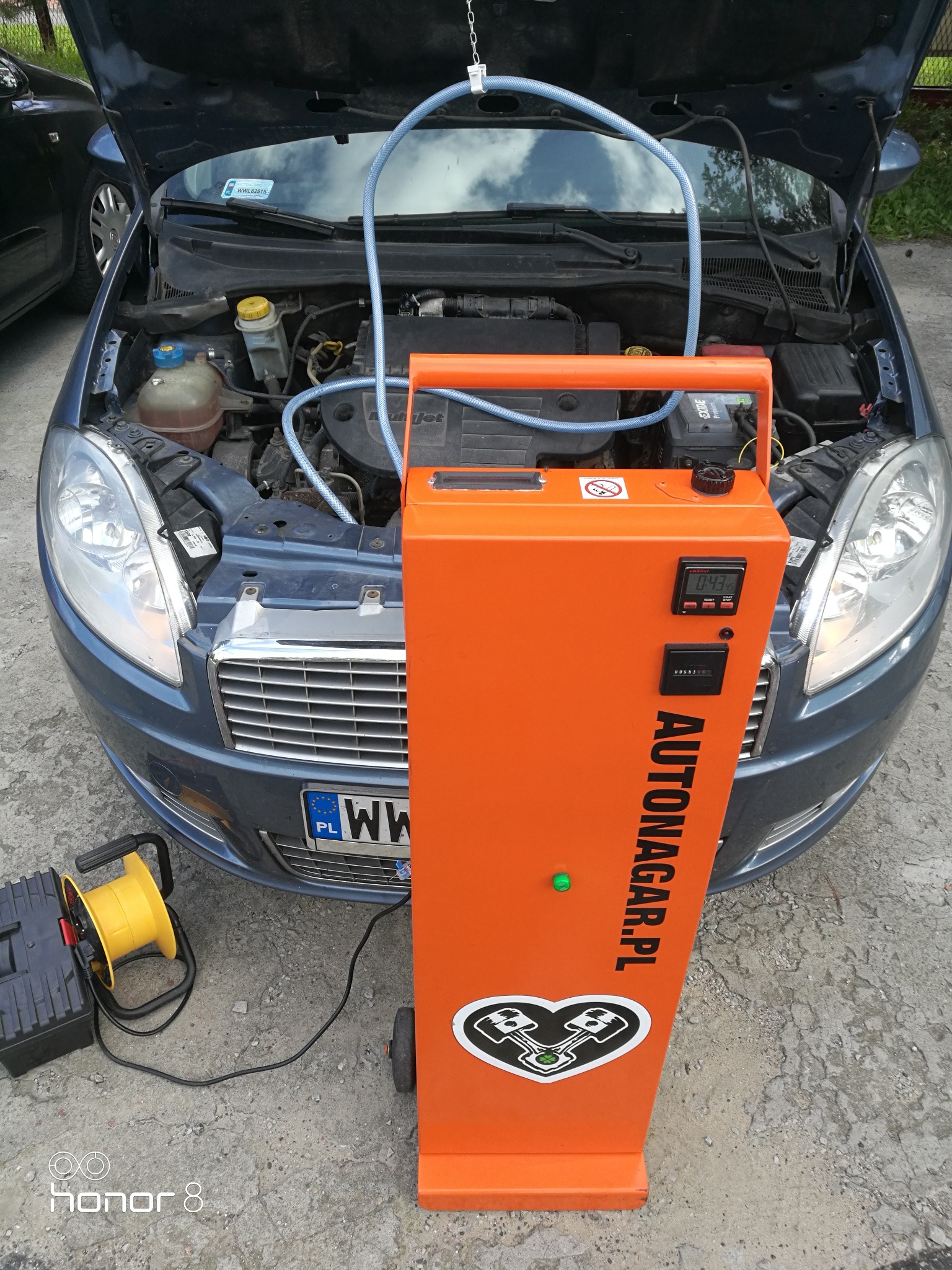 Wodorowanie silnika samochodu osobowego za pomocą pomarańczowego urządzenia Autonagar.pl z podłączonymi przewodami do otwartej maski pojazdu.