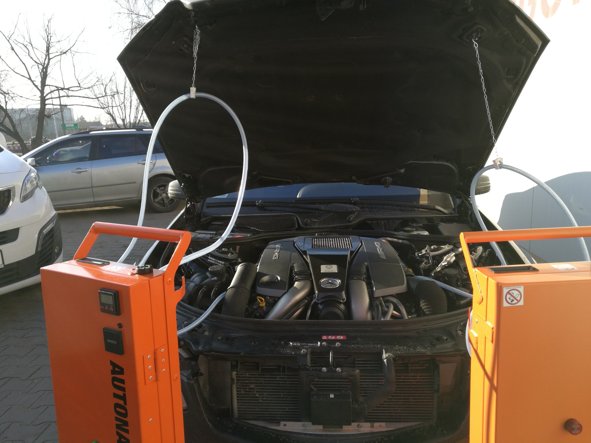 Silnik AMG w trakcie wodorowania za pomocą pomarańczowego urządzenia Autonagar.pl, widoczne przewody i otwarty przód samochodu.
