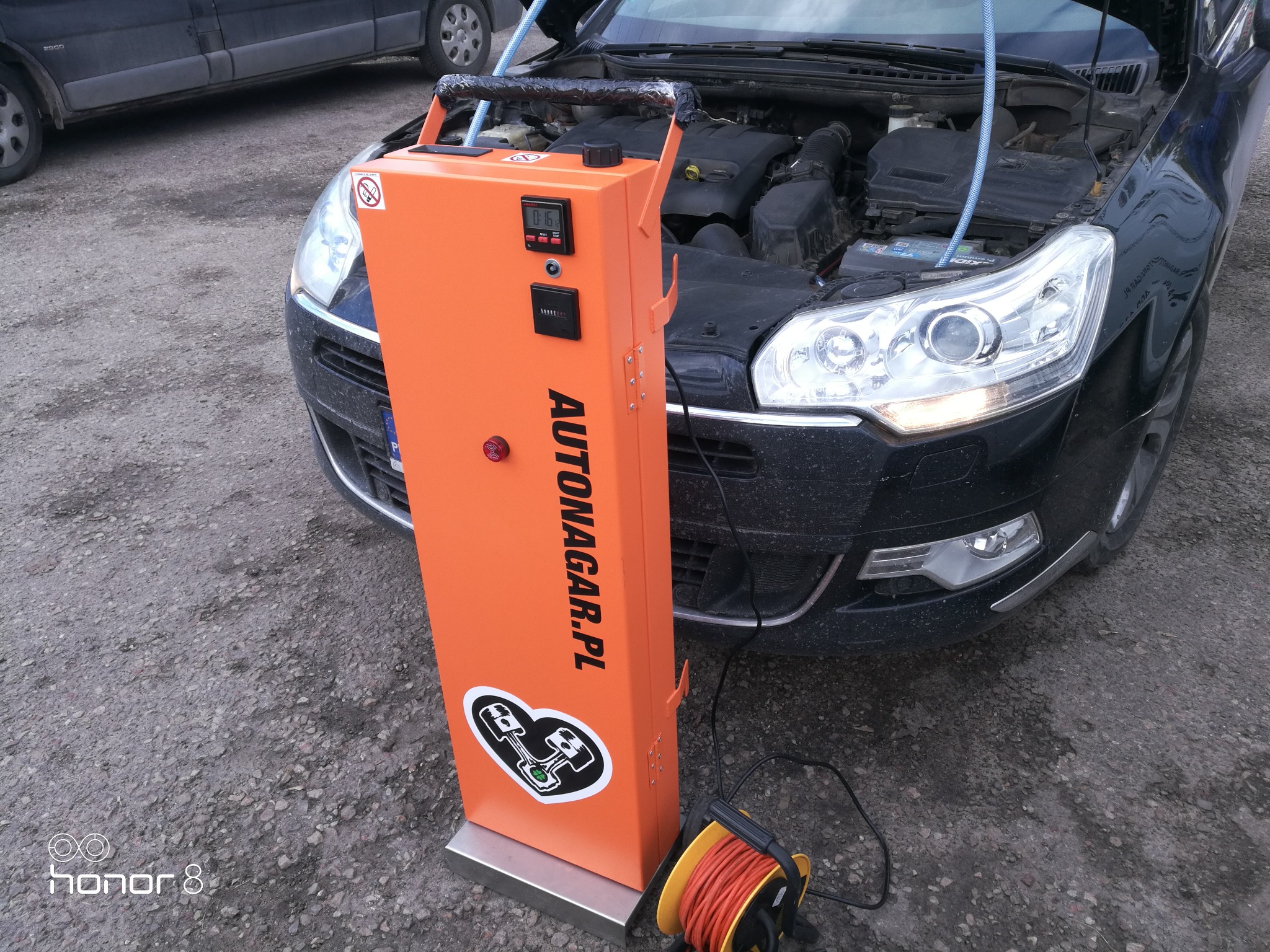 Wodorowanie silnika samochodu Citroen za pomocą pomarańczowego urządzenia Autonagar.pl z wyświetlaczem cyfrowym i naklejką z symbolem silnika w sercu, widoczne otwarte przednie maska i przewody...