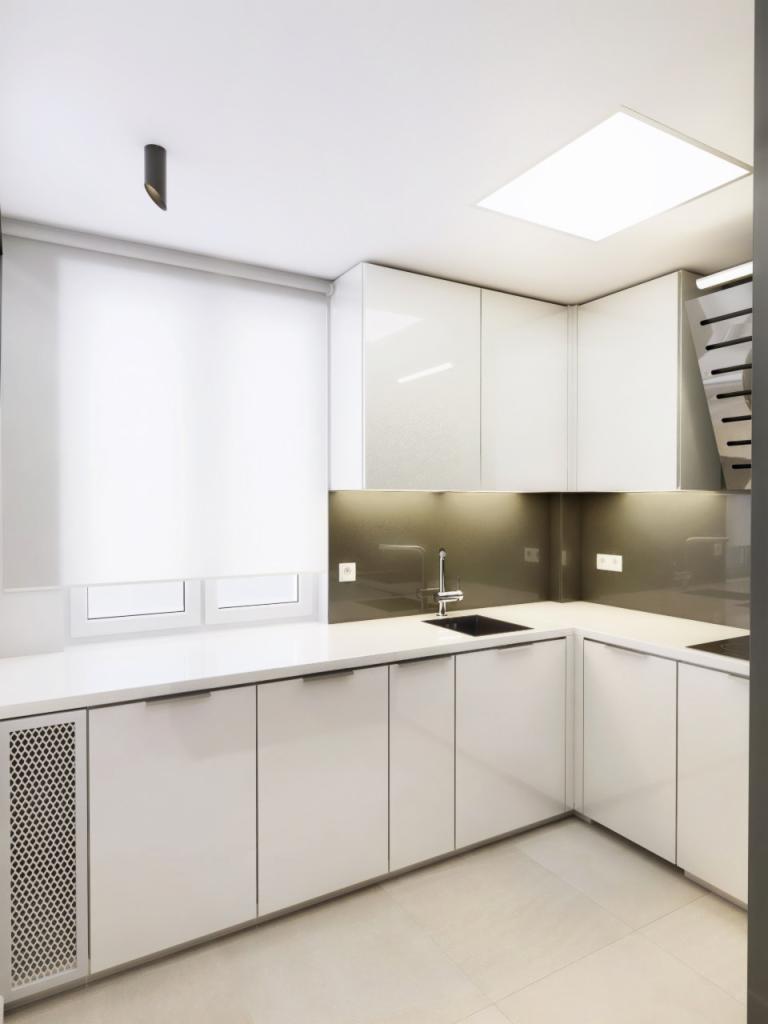 Nowoczesna, minimalistyczna kuchnia z białymi, błyszczącymi frontami szafek, czarnym zlewem i szarą ścianą nad blatem. W rogu widoczne schody.