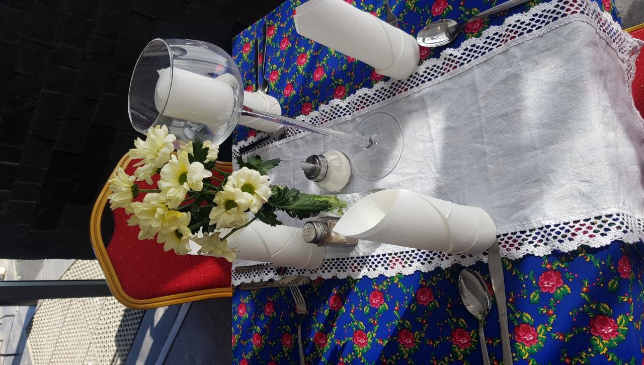 Uroczysty stół z białym obrusem z koronką, nakryty w stylu rustykalnym z kwiatami, świecą w szklanym kielichu, solniczką i pieprzniczką.