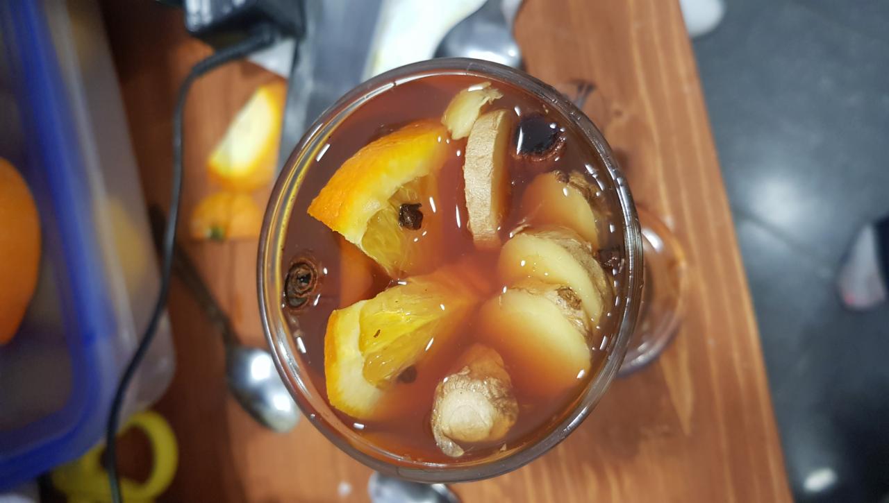Rozgrzewający napój w szklance z plastrami pomarańczy, imbirem i goździkami, widziany z góry na drewnianym blacie.