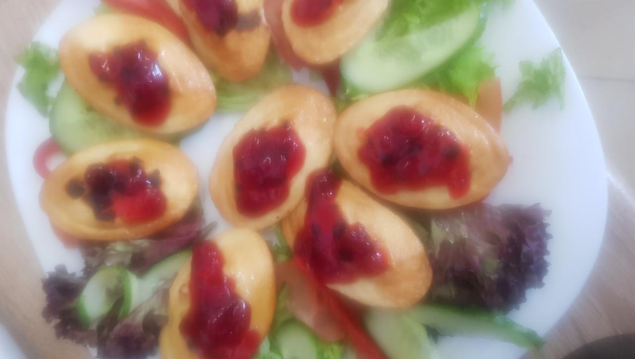 Talerz z mini omletami polanymi konfiturą, udekorowany świeżymi ogórkami, sałatą i papryką.