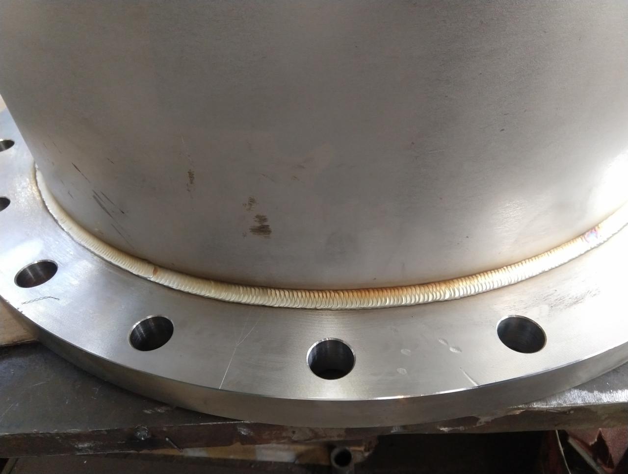 Szczegółowe ujęcie spoiny na rurze ze stali nierdzewnej z widocznymi otworami na śruby w kołnierzu.