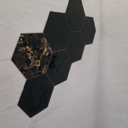 Ściana wyłożona białymi, podłużnymi płytkami z dekoracyjnym fragmentem z czarnych, heksagonalnych płytek, z których jedna posiada złoty, roślinny wzór.