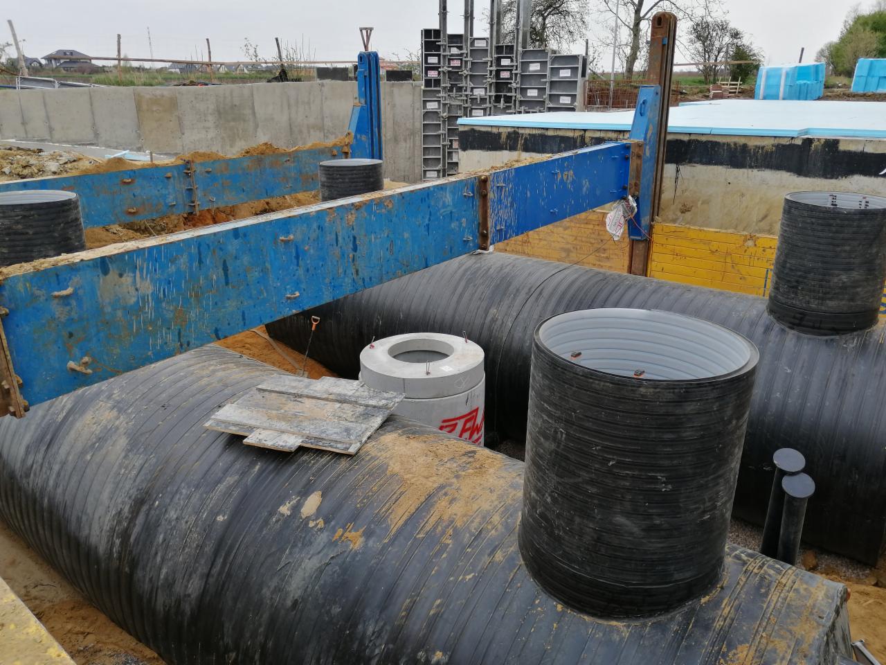Instalacja rur kanalizacyjnych w wykopie zabezpieczonym szalunkami, widoczne betonowe studzienki i elementy konstrukcyjne wykopu.
