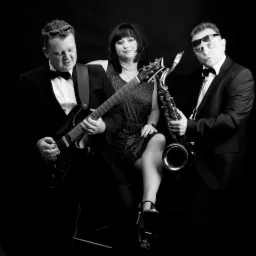 Czarno-białe zdjęcie tria muzycznego w formalnych strojach: gitarzysta gra na elektrycznej gitarze, wokalistka siedzi obok, a saksofonista trzyma saksofon, wszyscy w okularach przeciwsłonecznych.