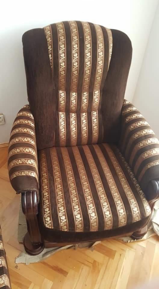 Brązowy fotel z tapicerką w pionowe pasy z motywem kwiatowym, drewniane nóżki, widoczne gniazdko elektryczne w tle.