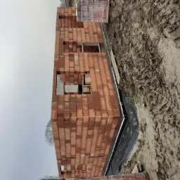 Wznoszenie ścian parteru z czerwonej ceramiki poryzowanej na budowie domu jednorodzinnego, widoczna hydroizolacja fundamentów i paleta z bloczkami