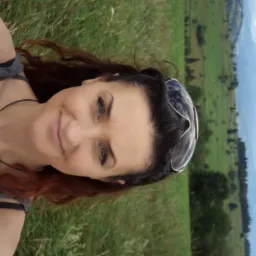 Uśmiechnięta kobieta z okularami na głowie robi selfie na tle zielonych wzgórz i błękitnego nieba z chmurami.