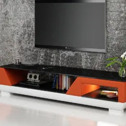 Nowoczesna szafka RTV z czarnym blatem i pomarańczowymi akcentami w salonie w Żywcu, z telewizorem na ścianie i białymi głośnikami po bokach.
