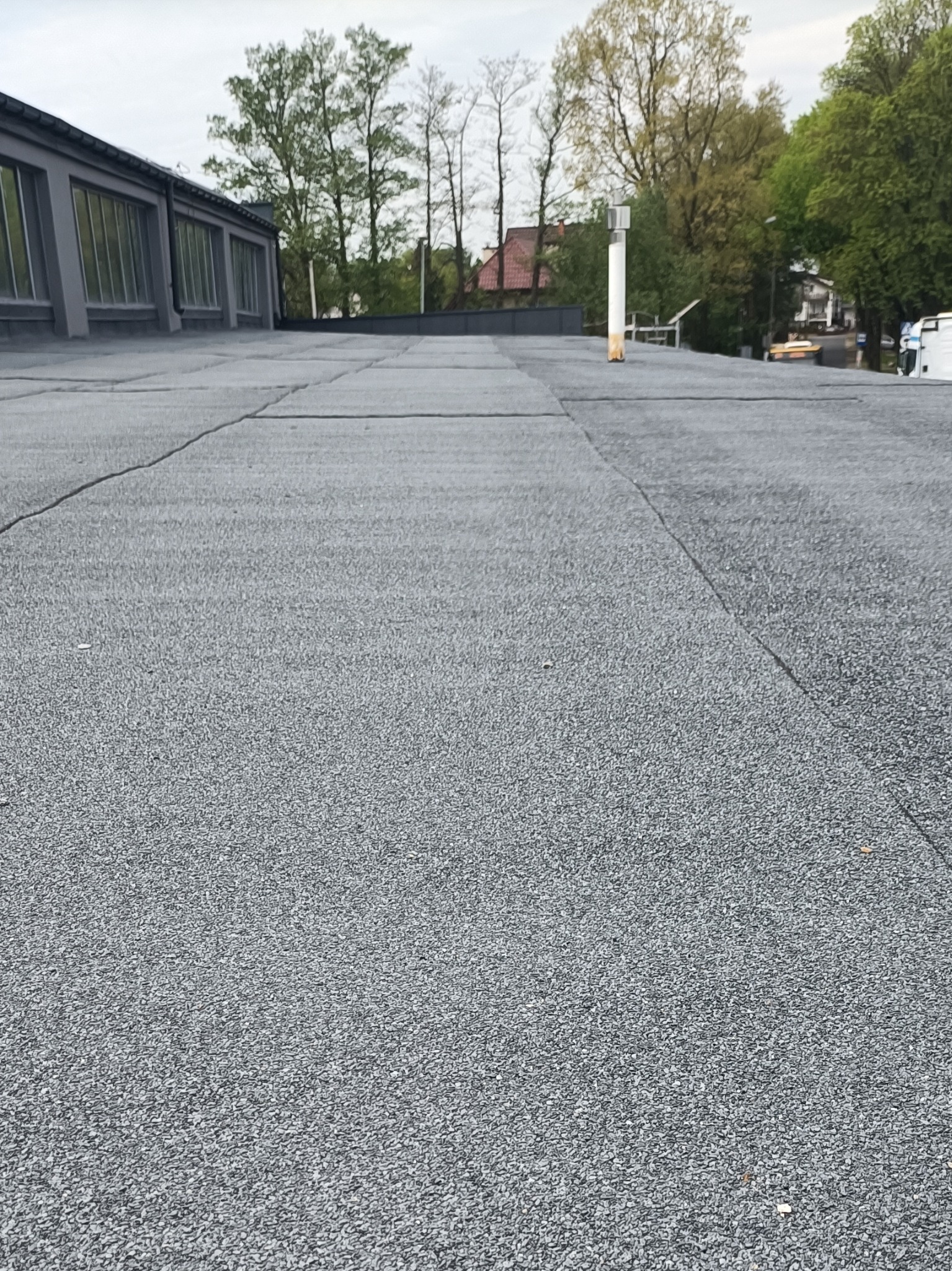 Szczelny dach pokryty papą termozgrzewalną w Warszawie, z widocznymi łączeniami i kominem wentylacyjnym. Widok z niskiej perspektywy, budynki w tle.