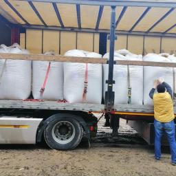 Midas Limited Sp.z o.o - Mężczyzna w żółtej kamizelce zabezpiecza ładunek worków w naczepie ciężarówki, widoczne pasy mocujące i drewniane podpory.