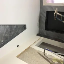 Ściana z wykończeniem w stylu betonu architektonicznego, widoczne rusztowanie i przygotowane otwory pod instalacje elektryczne.