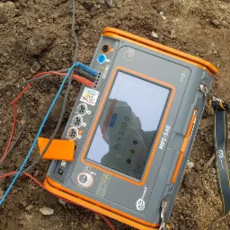 Miernik Sonel MPI-540 na ziemi z podłączonymi przewodami, wskazujący rezystancję 3,02 Ω. Urządzenie używane do pomiarów elektrycznych, widoczne złącza i ekran.