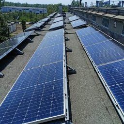 EMI GROUP - Instalacja paneli słonecznych na dachu budynku w Sędziszowie. Widok z góry na rzędy paneli fotowoltaicznych, z szarym dachem i elementami konstrukcyjnymi.