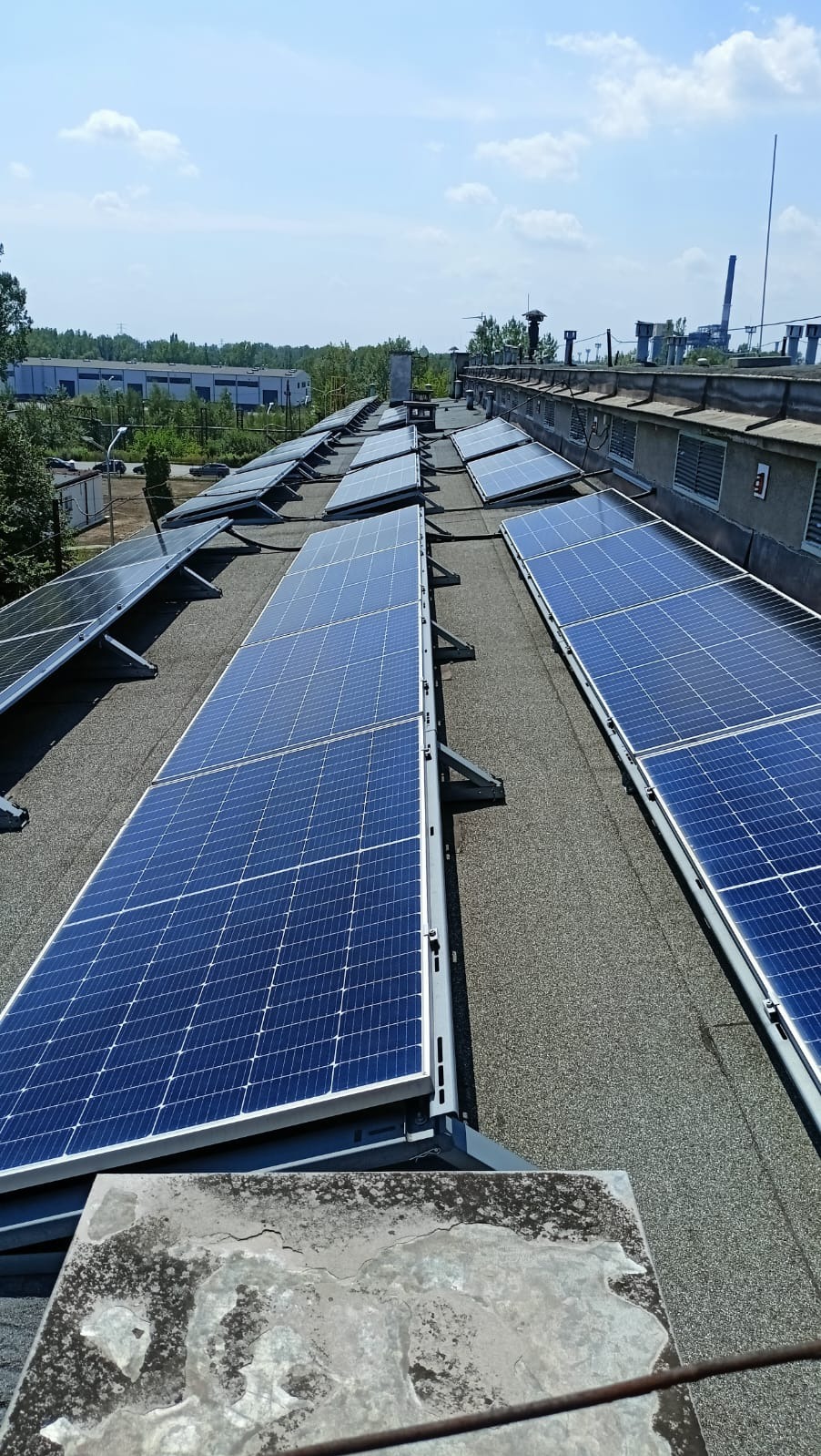 Instalacja paneli słonecznych na dachu budynku w Sędziszowie. Widok z góry na rzędy paneli fotowoltaicznych, z szarym dachem i elementami konstrukcyjnymi.