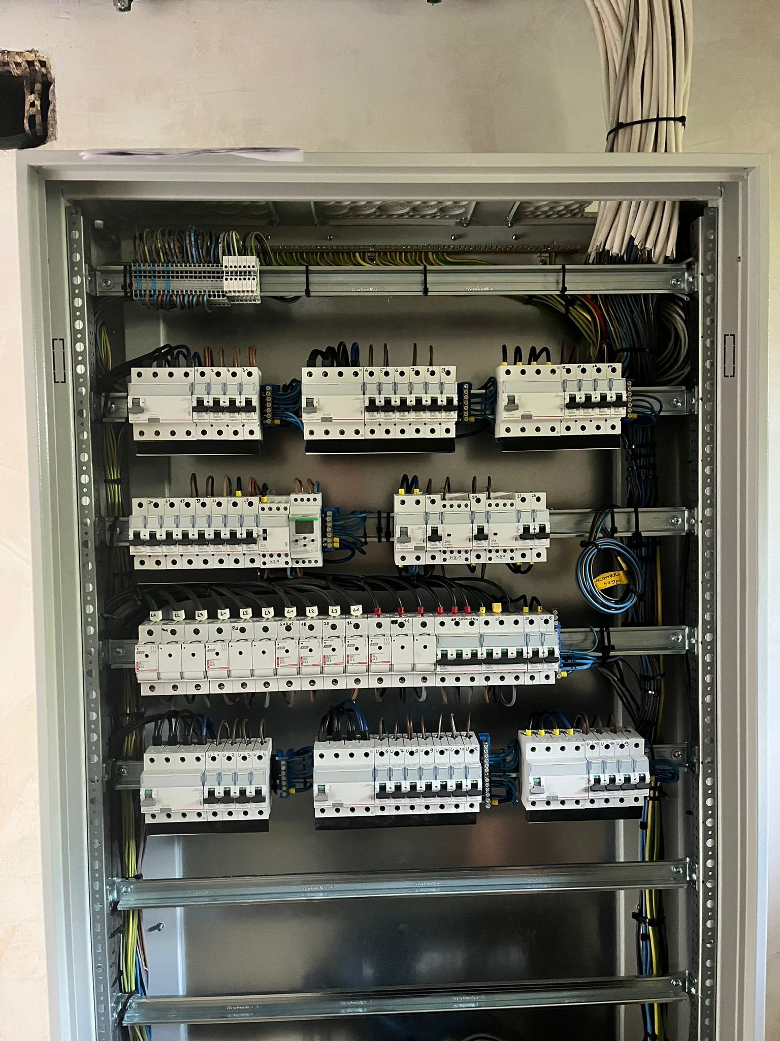 Rozdzielnica elektryczna w szarej obudowie, widoczne zabezpieczenia, przewody i szyny montażowe. Uporządkowany układ kabli na górze skrzynki.