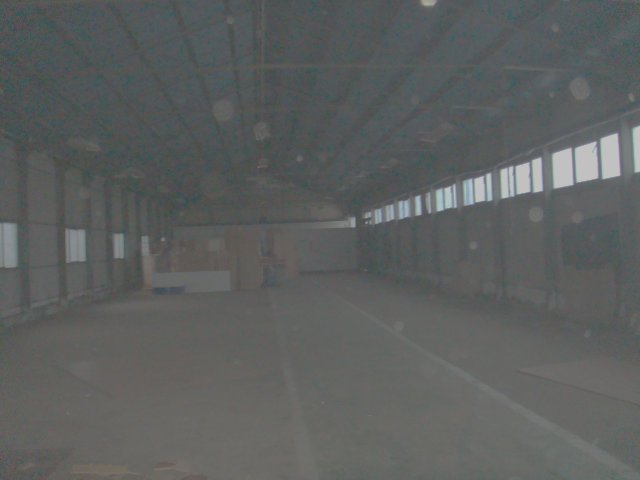 Wnętrze hali magazynowej o powierzchni 636m2 w Szczecinie Gumieńcach, z rzędem okien wzdłuż ściany i betonową podłogą, widok z głębi obiektu.