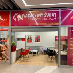 Wejście do biura podróży Dalex Holidays z widocznymi plakatami reklamowymi ofert wakacyjnych, ubezpieczeń turystycznych i rezerwacji hoteli, wnętrze z biurkami i krzesłami dla klientów.