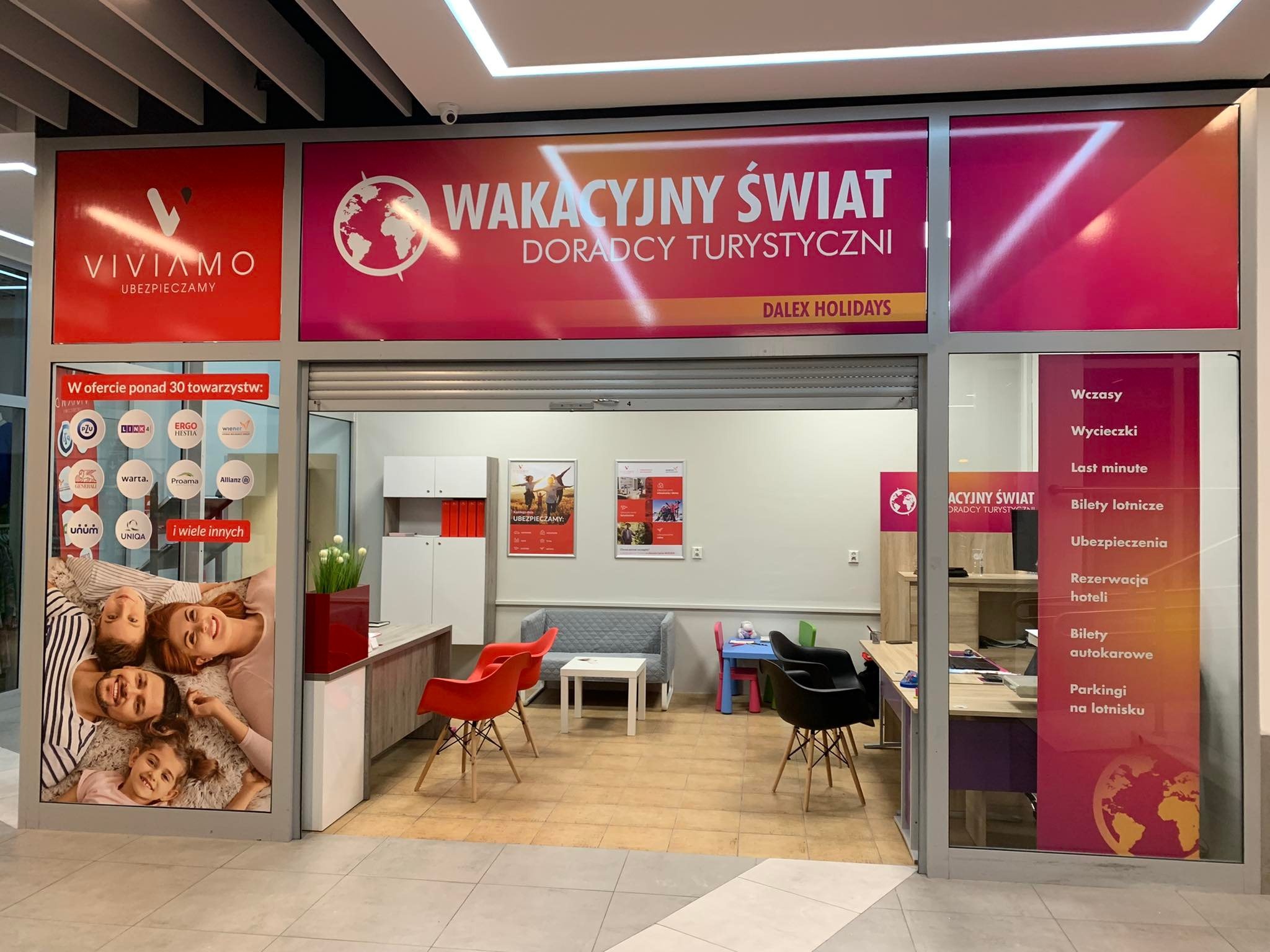 Wejście do biura podróży Dalex Holidays z widocznymi plakatami reklamowymi ofert wakacyjnych, ubezpieczeń turystycznych i rezerwacji hoteli, wnętrze z biurkami i krzesłami dla klientów.