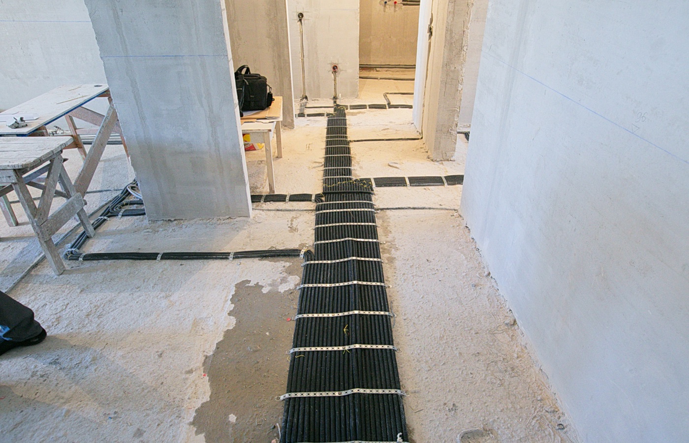 Wiązka czarnych kabli zabezpieczona metalowymi opaskami ułożona na surowym betonowym podłożu w trakcie prac instalacyjnych w budynku w stanie deweloperskim.