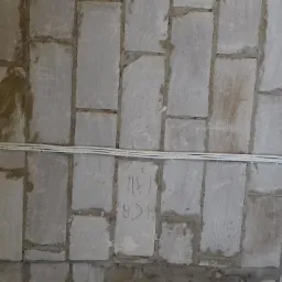 Kable elektryczne prowadzone po surowym, szarym murze z betonu komórkowego, zakończone czerwoną puszką instalacyjną z wyprowadzonymi przewodami.