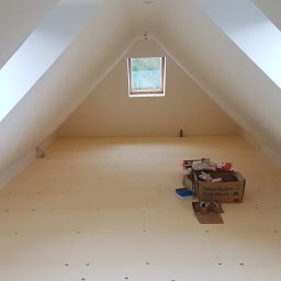 Usługi Ogólnobudowlane Suchecki Dariusz - Poddasze w trakcie wykańczania, widoczne płyty podłogowe z otworami, okno dachowe i kartonowe pudła z narzędziami.
