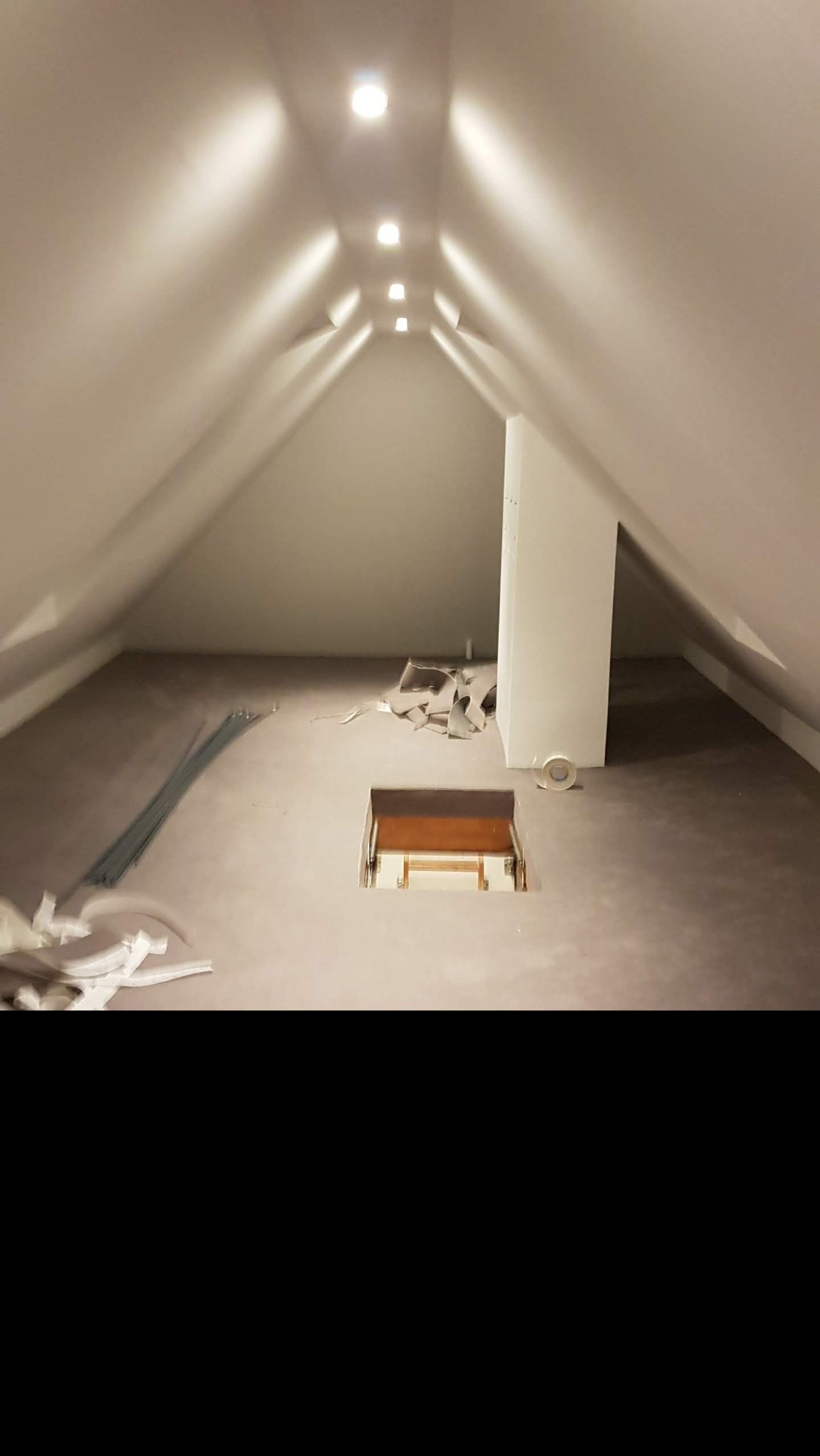 Poddasze z wykończonymi ścianami i sufitem, widoczne listwy i resztki materiałów po remoncie, otwór w podłodze z widocznymi schodami.