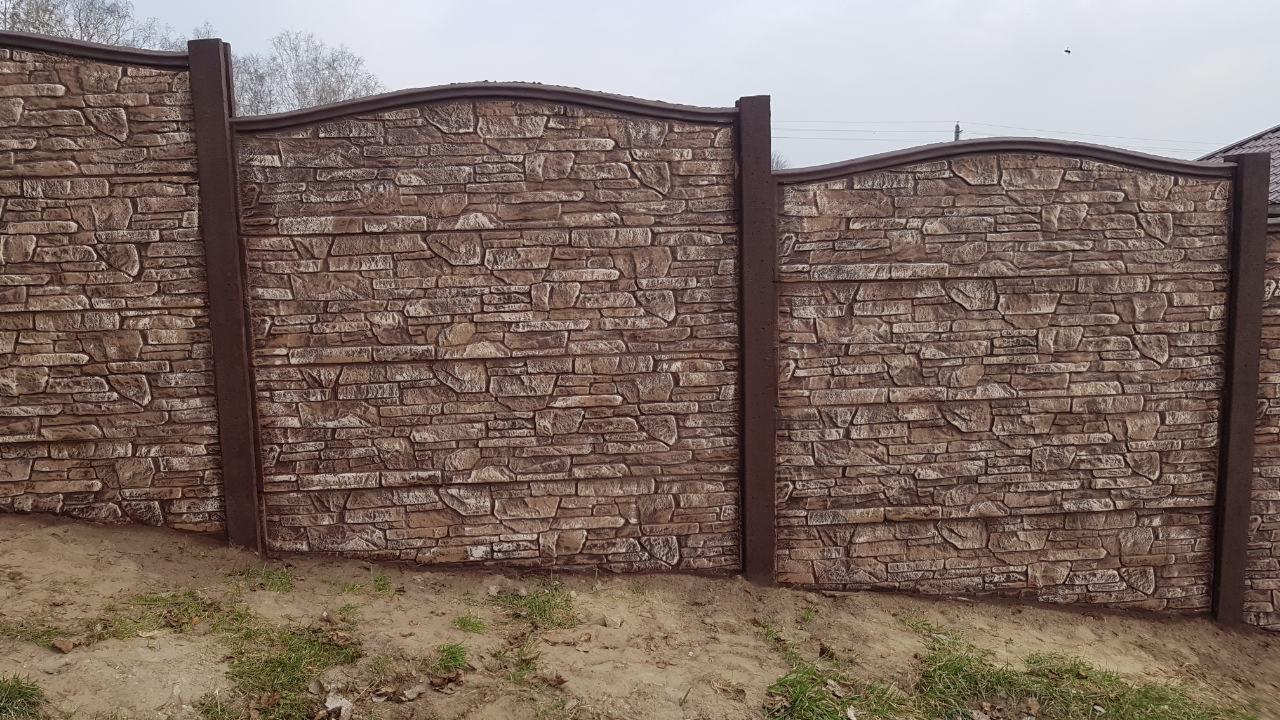 Panelowy płot z imitacją kamienia, brązowe słupki i górna listwa, lekko falista linia górna.