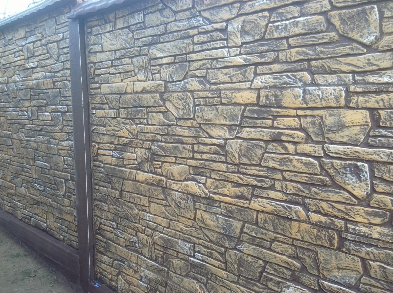 Nowoczesny, dekoracyjny płot betonowy imitujący kamień, z brązowymi elementami wykończeniowymi i słupkami.