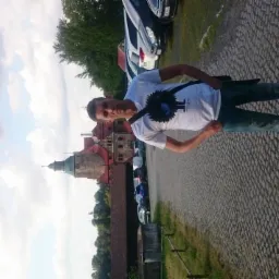 Mężczyzna w koszulce z grafiką na tle zamku i brukowanej drogi. Nietypowe ujęcie z elementami architektury i krajobrazu.