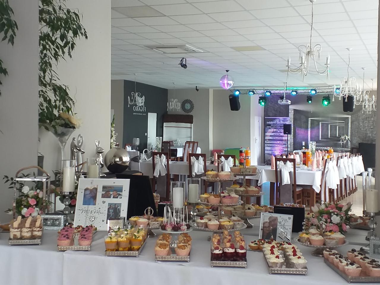 Stół z deserami i dekoracjami w sali bankietowej z parkietem i oświetleniem dyskotekowym w tle.