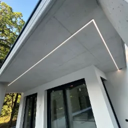 Nowoczesne oświetlenie LED podkreśla architekturę betonowego stropu nad oknami. Minimalistyczny design z precyzyjnie wkomponowanymi liniami świetlnymi.