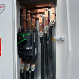 Rozdzielnia elektryczna z miedzianymi szynami, czarnymi kablami i wyłącznikiem Schneider Electric. Widoczne oznaczenia faz L1, L2, L3.  Szczegółowe ujęcie instalacji.
