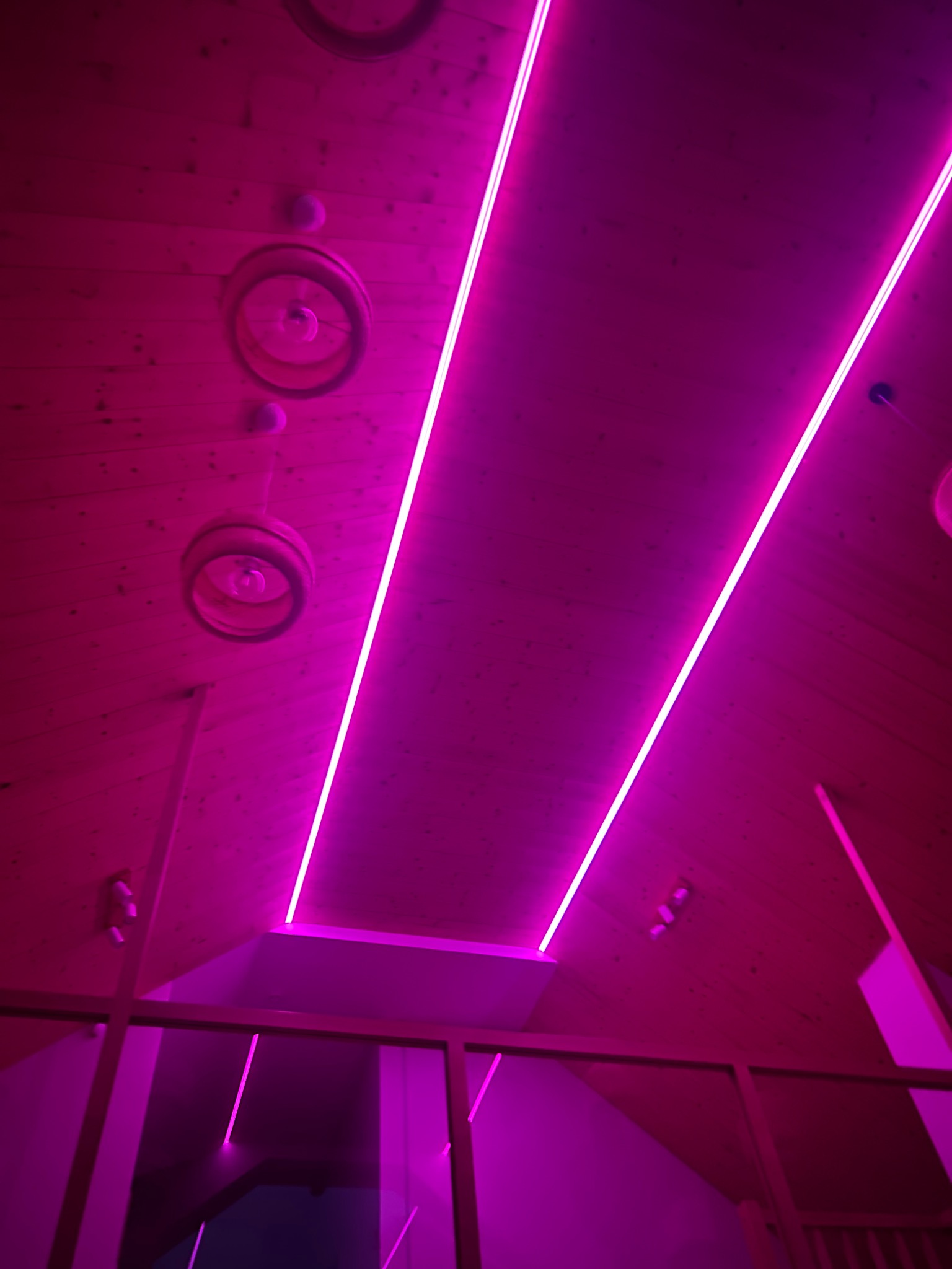 Nowoczesne oświetlenie sufitowe z drewnianym wykończeniem i neonowymi lampami w odcieniach fuksji, tworzące unikalny klimat wnętrza.