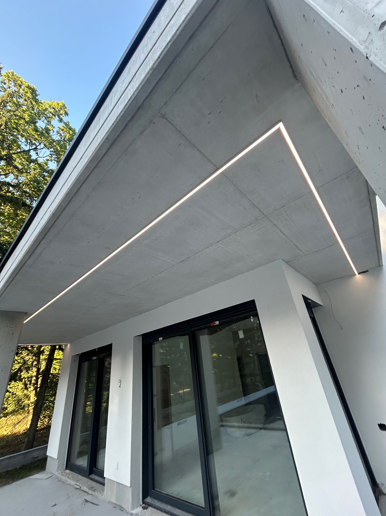 Nowoczesne oświetlenie LED podkreśla architekturę betonowego stropu nad oknami. Minimalistyczny design z precyzyjnie wkomponowanymi liniami świetlnymi.