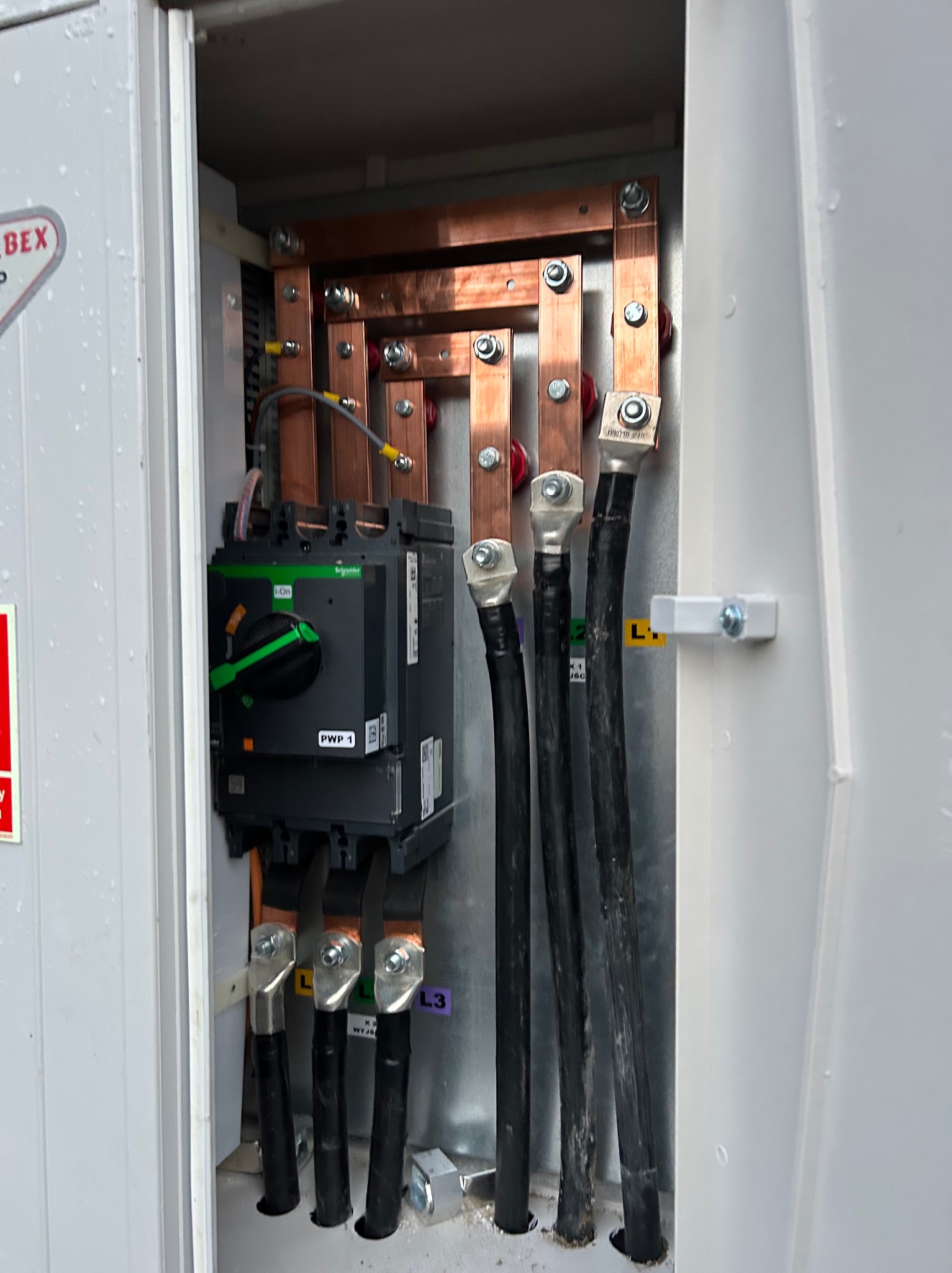 Rozdzielnia elektryczna z miedzianymi szynami, czarnymi kablami i wyłącznikiem Schneider Electric. Widoczne oznaczenia faz L1, L2, L3.  Szczegółowe ujęcie instalacji.