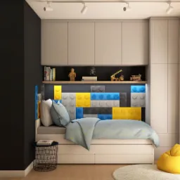 Pokój dziecięcy z łóżkiem wbudowanym w ścianę z motywem klocków Lego w kolorach niebieskim, żółtym i szarym, półka z książkami i zabawkami, oraz żółta pufa na okrągłym dywanie.