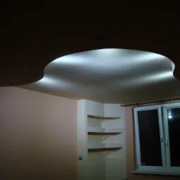 Nietypowy sufit podwieszany z oświetleniem punktowym i wnęką w kształcie nerki, ściana w odcieniach beżu, wnęka z półkami i okno.