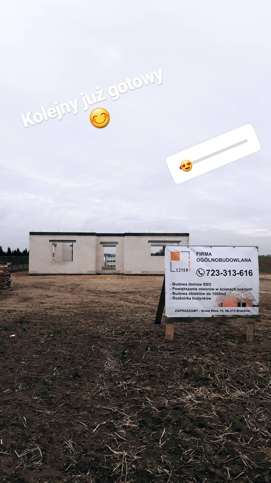 Dom w stanie surowym otwartym z bloczków H+H, z widoczną tablicą reklamową firmy budowlanej na pierwszym planie, ziemiste podłoże.