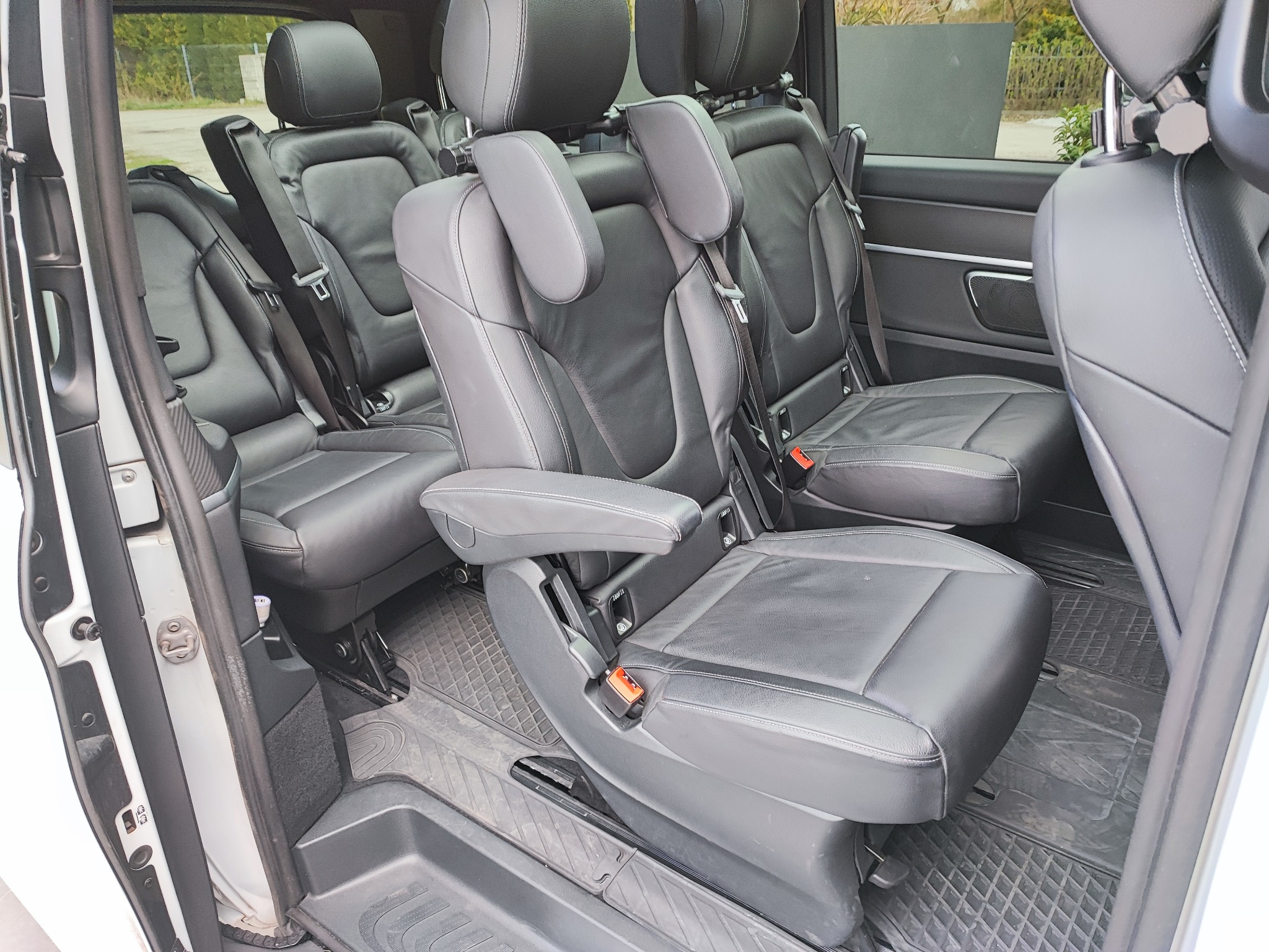 Wnętrze luksusowego busa z trzema rzędami skórzanych foteli, widok z boku na rozłożony podłokietnik i gumową wycieraczkę pod nogami.