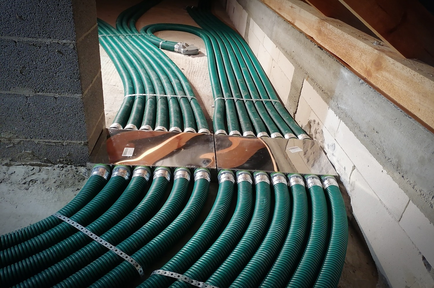 Rozprowadzona instalacja wentylacyjna z zielonych, karbowanych rur w surowym wnętrzu budynku, widoczne metalowe skrzynki rozdzielcze i fragmenty ścian z betonu komórkowego.