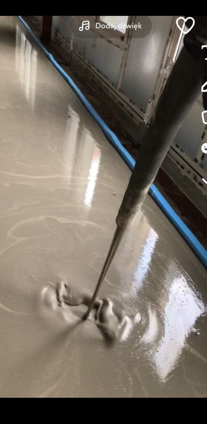 Wylewka samopoziomująca rozprowadzana w pomieszczeniu biurowym, widoczny wąż do wylewki i niebieski profil przyścienny.