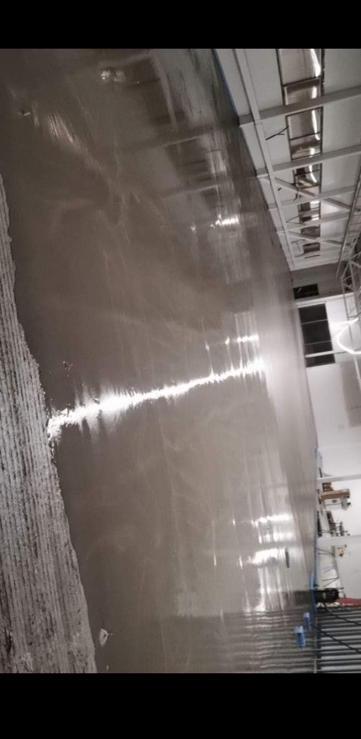 Wylewka samopoziomująca na podłodze w przestrzeni biurowej, widoczne refleksy światła, surowy stan wykończenia.