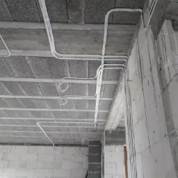 Białe przewody elektryczne ułożone na surowym, betonowym suficie i ścianach z białych bloczków w trakcie prac instalacyjnych.