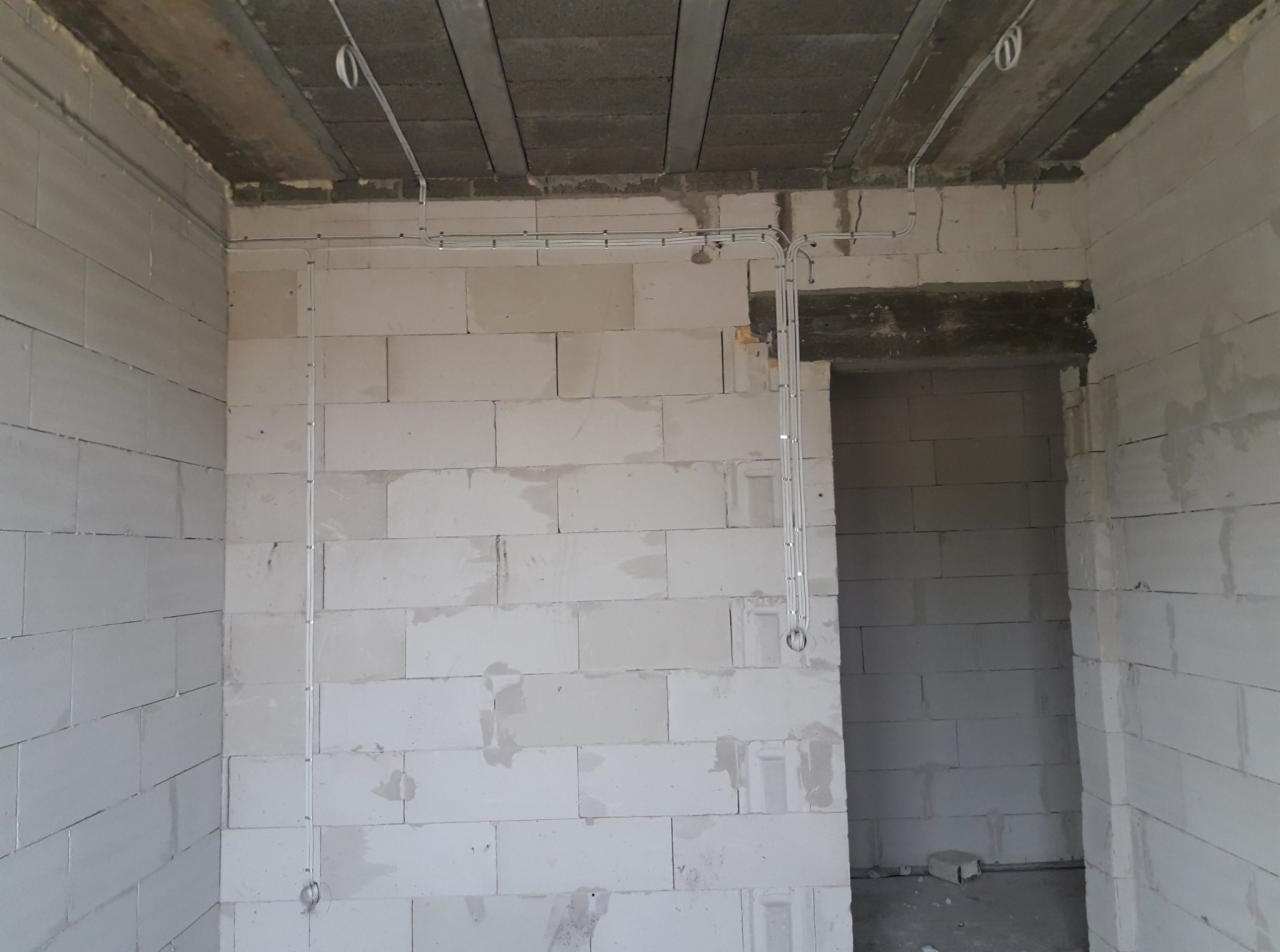 Wnętrze surowego budynku z widocznymi przewodami elektrycznymi poprowadzonymi po ścianach z białych bloczków, oraz pod sufitem, przed tynkowaniem.