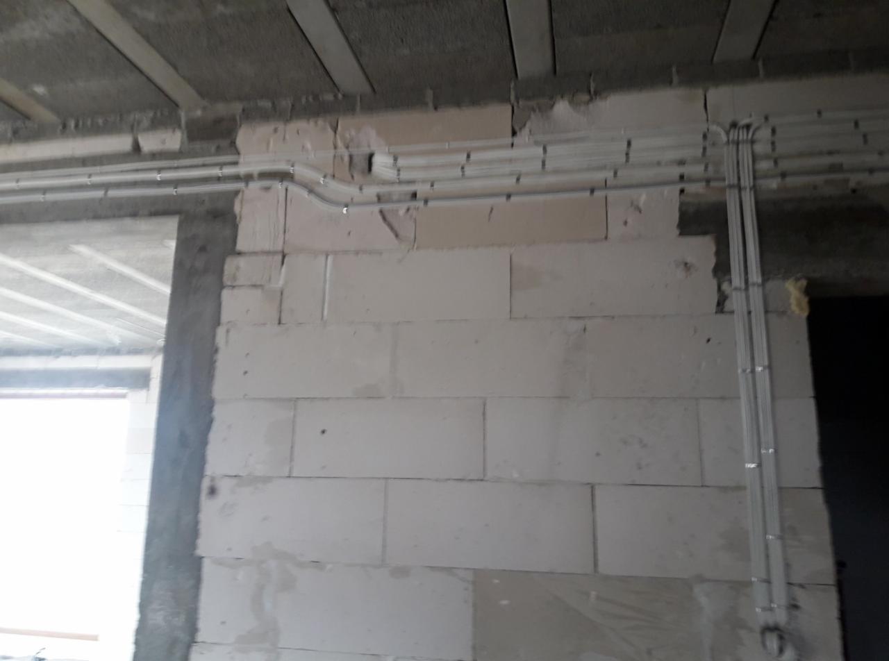 Montaż instalacji elektrycznej w surowym stanie: kable w białych listwach prowadzone po ścianie z betonu komórkowego, widoczne niedoskonałości tynku.