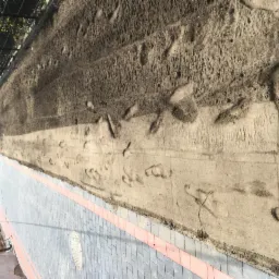 Przygotowanie terenu pod trawnik z rolki: wyrównana ziemia z widocznymi śladami stóp, sąsiadująca z nową kostką brukową z czerwoną obwódką.