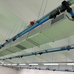 GoHVAC - Kompletna instalacja wentylacji mechanicznej z izolowanymi kanałami PIR, niebieskimi rurami i czerwonymi gniazdami, zamontowana pod sufitem w jasnym pomieszczeniu.